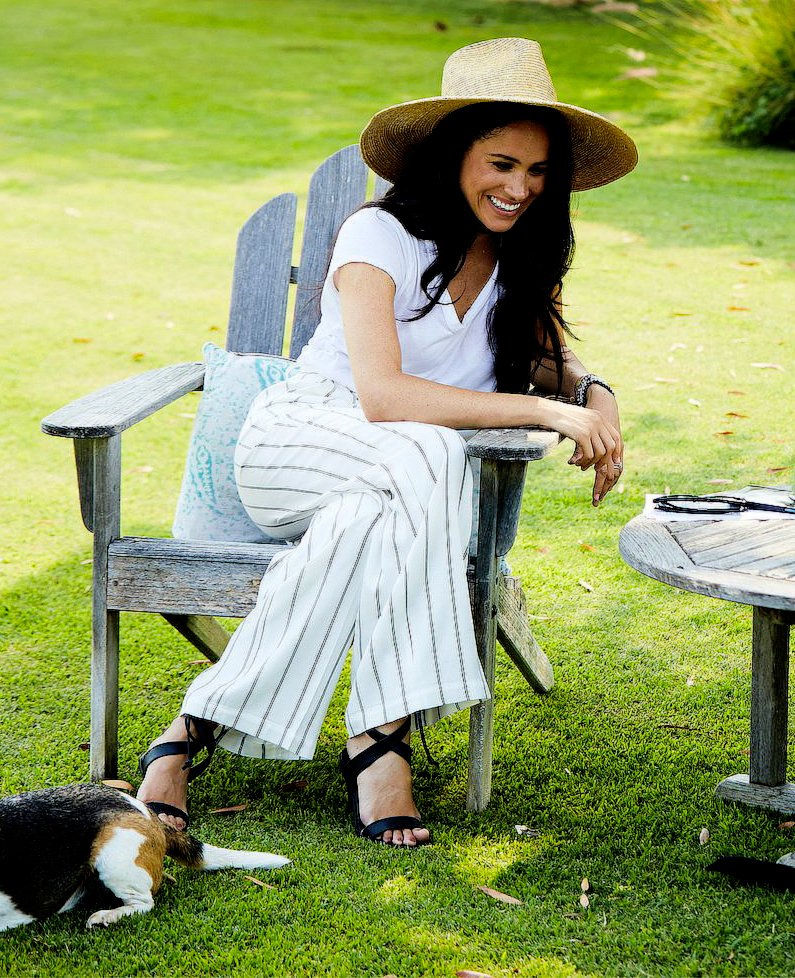 Meghan Markle wore a white tee teamed with Anine Bing Ryan striped trousers, Stella McCartney black Rhea sandals and Janessa Leone Serena Hat